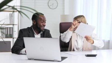 Two people analyze documents on a laptop while sitting at a table in the office. Business partners man and woman.Multi-racial collaboration. The joy of a successful deal, contract