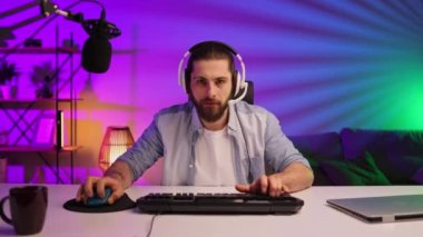 Gamer bearded guy, in a gaming headset, wins a video game. Cybersportsman in a neon room. Lifestyle gamer, online games. Victory in the E-Sport tournament.