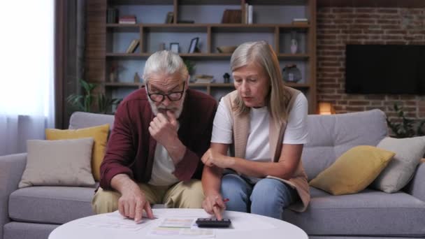 白髪の退職したカップルは 計算機上の光熱費の計算について心配しています エネルギーおよびガス料金のための大きい費用 人口のためのエネルギー危機 — ストック動画