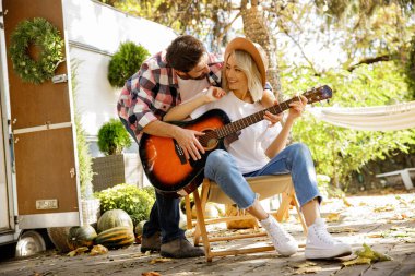 Komik ve neşeli genç bir çift. Adam bir seyahat karavanının arka planında gitar çalıyor, şarkı söylüyor ve dans ediyor. Şehrin dışında dinlen. Mutlu insanlar eğlenir. Yazın hafta sonları
