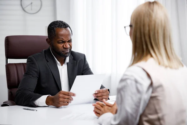 Hiring, interview. Middle aged business african american boss holding a job interview in a bright office. He looks at the resume, he does not like the employee. Refuses to apply for a job