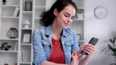 Young curly brunette sitting at the table uses a mobile phone. Surfs the Internet, communicates in instant messengers on his smartphone. Online communication, smartphone in human life