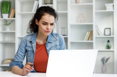 A young curly-haired brunette student sits at a table and uses a laptop for learning. Online school, remote work, programmer or manager. The concept of remote work or learning.