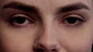 Kahverengi gözlü, doğal makyajlı ve uzun kirpikli genç kız doğrudan kameraya bakıyor. Kadınların yüzlerine yakın çekim