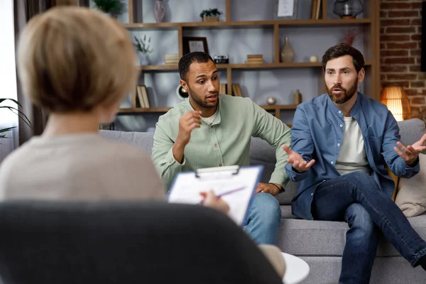 A family psychologist conducts a session in a beautiful office. LGBT couple at a psychotherapists appointment. Psychologist for gays. Support for the LGBT community in visiting a psychologist