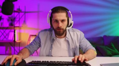 Gamer bearded guy, in a gaming headset, wins a video game. Cybersportsman in a neon room. Lifestyle gamer, online games. Victory in the E-Sport tournament.