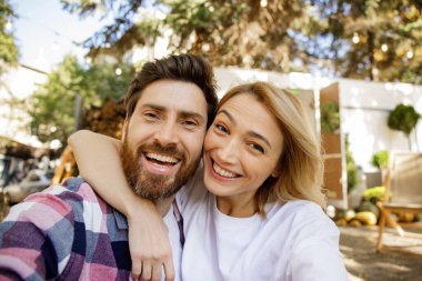 Sevimli bir çift seyahat karavanının yanında oturmuş selfie çekiyor, gülüyor, eğleniyor ve tatillerinin tadını çıkarıyorlar. Şehir dışında güneşli bir günün tadını çıkaran bir aşk portresi, kamera görüntüsü.