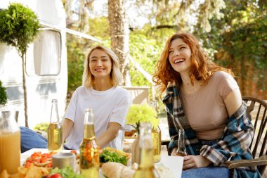 İki arkadaş piknik masasında eğleniyor. Sarışın ve kızıl saçlı bir kız şehrin dışındaki ormanda piknik yapıyorlar.