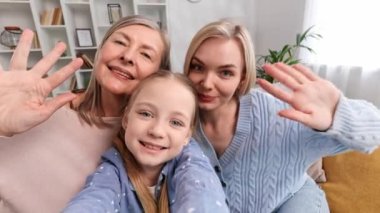 Mutlu büyükanne, anne ve torun oturma odasındaki kanepede oturup selfie çekiyorlar, akrabalarıyla görüntülü görüşme yapıyorlar, el sallıyorlar. Anneler Günü için tebrikleri dinliyorlar.