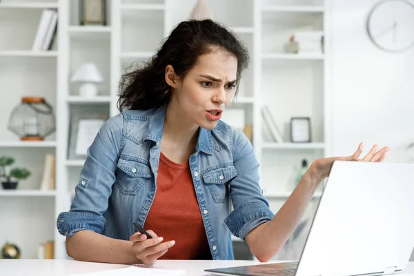 Disappointed girl looks at the laptop screen, does not understand what happened. Brunette woman is angry that the computer broke