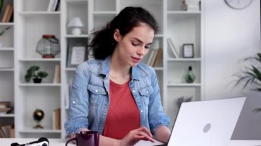 A young curly-haired brunette student sits at a table and uses a laptop for learning. Online school, remote work, programmer or manager. The concept of remote work or learning.