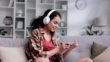 Kıvırcık saçlı kız öğrenci kanepeye oturur, kulaklık takar, not defterine kalemle yazar ve telefon bildirimlerini kontrol eder. Güzel bir kadın çalışır ve çalacak müziği değiştirir..