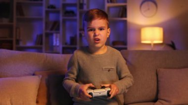 Video oyunu oynayan mutlu bir çocuğun portresi, evde kameraya dikkatlice bakan bir joystick ile çok zor. Oyun ve çocukluk kavramı