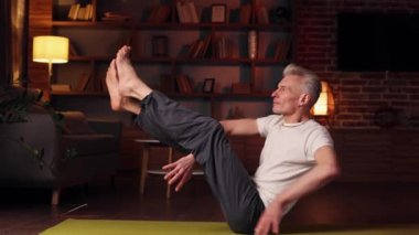 Yoga at home. The gray-haired man does yoga at home, doing asanas. Sports, stretching, gymnastics of an elderly man. Healthy lifestyle in old age