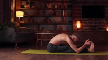 Yoga at home. The gray-haired man does yoga at home, doing asanas. Sports, stretching, gymnastics of an elderly man. Healthy lifestyle in old age