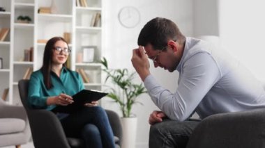 Profesyonel bir psikolog, ofiste bir sandalyede oturan, stres ve depresyon halinde olan bir erkek hastaya danışıyor. Kağıda yazıyor. Danışman psikolog konsepti