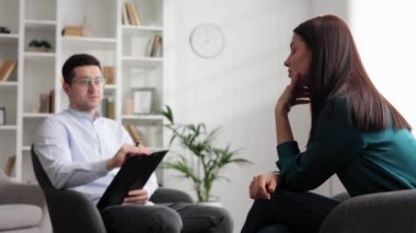 Profesyonel bir psikolog, ofiste bir sandalyede oturan stres ve depresyon durumundaki bir kadın hastaya danışıyor. Kağıda yazıyor. Danışman psikolog konsepti