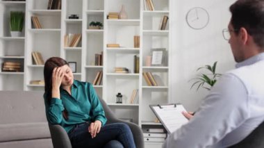 Profesyonel bir psikolog, ofiste bir sandalyede oturan stres ve depresyon durumundaki bir kadın hastaya danışıyor. Kağıda yazıyor. Danışman psikolog konsepti