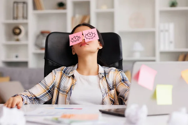 The concept of a lot of work. Tired Indian student girl sleeping with stickers on her eyes while sitting at the table. Distracted woman in home office