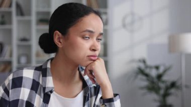 Çekici Afrikalı Amerikalı kız oturma odasında oturuyor, yanak yanağa dinleniyor, yorgun görünüyor. Üzgün genç kız olumsuz düşüncelerden muzdarip, depresyonda ilişki sorunları var, hatalarından pişman.