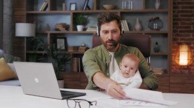 Father on maternity leave, holding an online conference, a meeting in the home office with a small child in his arms. Dad with a child. Freelancer combines child care and work. Paternity leave.
