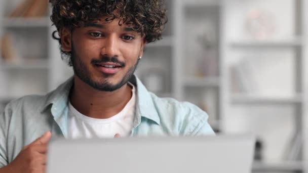 一位蓄着胡子的专注的印度男性商人正在客厅的笔记本电脑前学习 一个年轻人认真地听一个视频会议 在笔记本上写下信息 — 图库视频影像