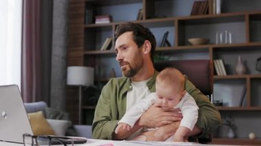 Father on maternity leave, holding an online conference, a meeting in the home office with a small child in his arms. Dad with a child. Freelancer combines child care and work. Paternity leave.