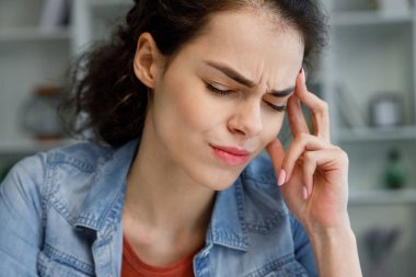 Genç kıvırcık esmer kadın masada stresli bir şekilde oturuyor, iş yerinde aşırı çalışmaktan dolayı ilgisizlik ve depresyon hissediyor. Modern dünyadan tükenmiş. Hayattaki sorunlar, kötü haberler. Baş ağrısı, migren.