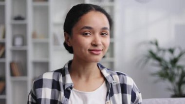 Evdeki kanepede oturan, başını kameraya çevirip gülümseyen Afro-Amerikan bir kızın portresi.