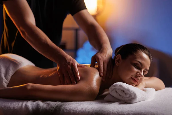 A young brunette woman receives a professional back massage in a spa salon. A beautiful naked lady in a towel with perfect skin gets a relaxing massage. The concept of luxury professional massage