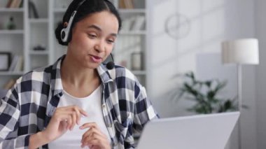 Kulaklık takmış genç bir Afro-Amerikalı iş kadını video aracılığıyla iletişim kuruyor. Laptop bilgisayarına bakarken konuşan etnik kız öğrenci, çevrimiçi ofis konferansı, sanal öğrenim kavramı