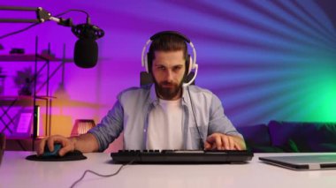 Cybersportsman in a neon room. Gamer bearded guy, in gaming headphones, challenges. Lifestyle gamer, online games. E Sports.