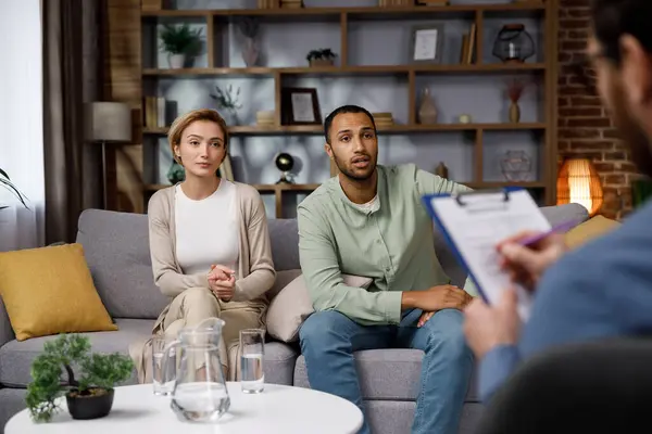 Multiracial quarrel between husband and wife at a session with a psychotherapist. A visit to a family psychologist for a married couple. A doctor consults an unhappy married couple. Help psychologist