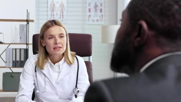 女性医師はアフリカ系アメリカ人男性の患者を事務所で受け取っている 医師相談 — ストック動画