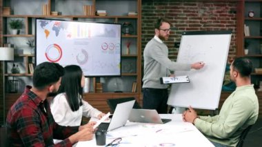 Takım lideri gülümseyen genç çokuluslu meslektaşlarına şirket geliştirme stratejisini açıklıyor. Mutlu çok ırklı iş adamları ofiste birlikte çalışmaktan hoşlanırlar. Başlangıç çalışması