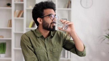 Genç bir Hintli çocuk oturma odasındaki masada oturuyor ve yeni bir güne iyi bir alışkanlıkla başlıyor, bir bardak temiz su tutuyor ve içiyor, yakından bakıyor.