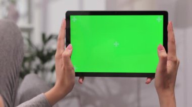 Kanepede yatay konumda tablet kullanarak uzanan kızın yakın plan çekimi. Parlak odada yeşil ekran modeli ile video izlerken farklı jestler kullanırken.