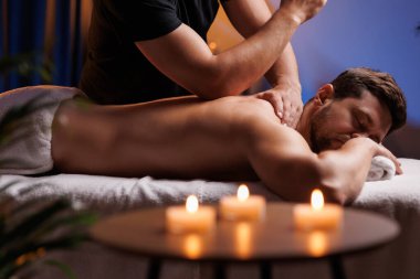 Yakışıklı bir adam spa salonunda sırt masajı yaptırıyor, rahatlatıcı atmosferin tadını çıkarıyor, işten sonra şarj oluyor. Masöz, ziyaretçilere terapötik sırt masajı yapar. Sağlıklı yaşam tarzı kavramı.
