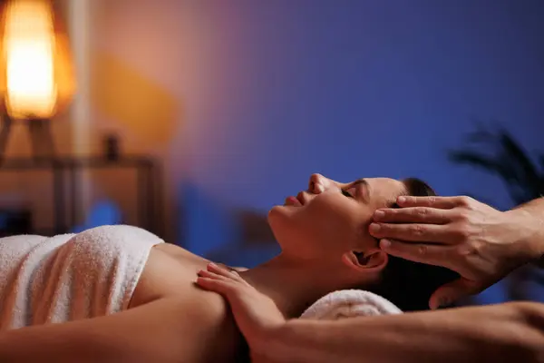 A young brunette woman receives a professional head and shoulders massage in a spa salon. A beautiful lady in a towel with perfect skin gets a relaxing massage. The concept of luxury professional