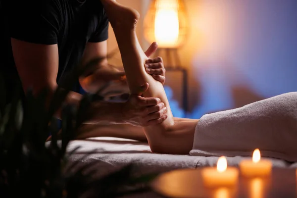 Masseuse makes an anticellulite relaxing foot massage in a spa for a young girl in a comfortable atmosphere with evening light. Therapeutic foot massage, recovery after injuries, health maintenance
