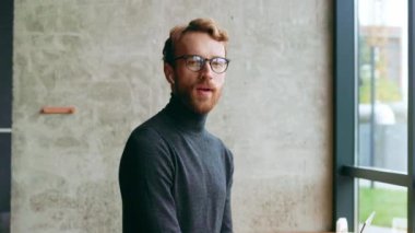 Genç kızıl saçlı bir adam, bir programcı ya da gözlüklü bir girişimci şık bir kafede kameraya bakar ve gülümser. Freelancer uzaktan çalışıyor. Çevrimiçi iletişim. küçük işletme