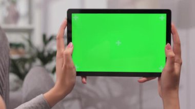 Kanepede yatay konumda tablet kullanarak uzanan kızın yakın plan çekimi. Parlak odada yeşil ekran modeli ile video izlerken farklı jestler kullanırken.