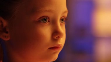 Güzel küçük bir kızın portresi akşamları evde oturur düz bakar, göz kırpar. Yakın çekim, detaylı gözler, yüz profili.