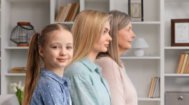 Genç anne ve büyük anneyle evde poz veren sevimli küçük kız, yan görünüm, yakın plan portre. Yaşam süresi, yeni nesil, döllenme ve kalıtım. Anneler Günü için.