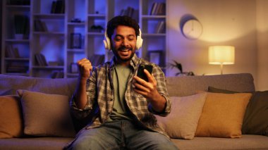 Sakallı genç bir adam oturma odasında kanepede oturarak piyangoyu kazanmaktan mutlu. Mutlu adam telefondaki e-postayı kontrol ediyor ve iyi haberlerle mutlu.