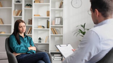 Profesyonel bir psikolog, ofiste bir sandalyede oturan stres ve depresyon durumundaki bir kadın hastaya danışıyor. Kağıda yazıyor. Danışman psikolog konsepti