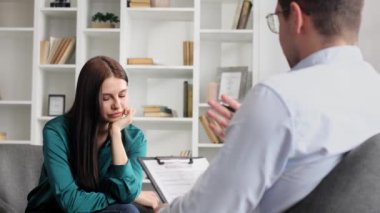 Profesyonel bir psikolog, ofiste bir sandalyede oturan stres ve depresyon durumundaki bir kadın hastaya danışıyor. Kağıda yazıyor. Danışman psikolog konsepti