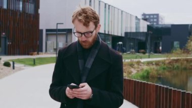 Genç kızıl saçlı bir adam, gözlüklü bir işadamı, şehir tarzının arka planına karşı, akıllı bir telefondan postaları kontrol ediyor, kurye ile iletişim kuruyor ve kahve içiyor. Çevrimiçi iletişim
