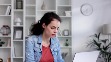 A young curly-haired brunette student sits at a table and uses a laptop for learning. Online school, remote work, programmer or manager. The concept of remote work or learning.