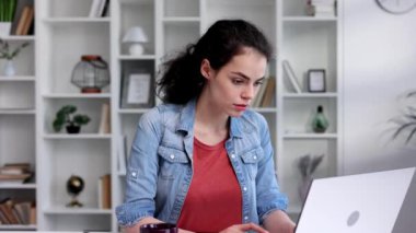 A young curly-haired brunette student sits at a table and uses a laptop for learning. Online school, remote work, programmer or manager. The concept of remote work or learning.